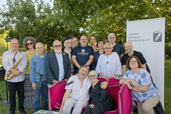 Zwölf Poet:innen, zwei Moderator:innen und ein Musiker lächeln fürs Gruppenfoto in die Kamera